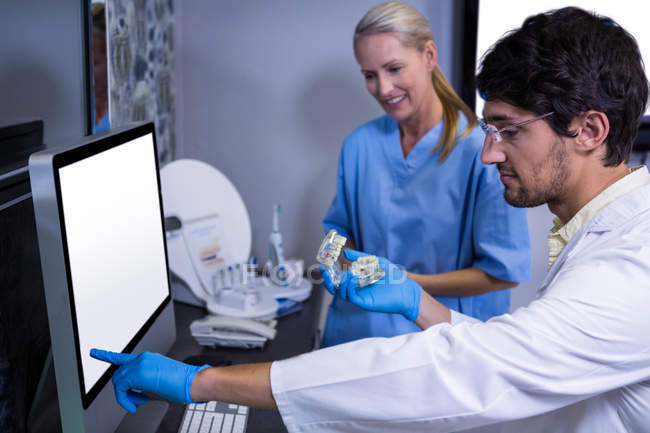 Стоматолог та стоматолог використовують комп'ютер під час роботи над моделлю рота — стокове фото