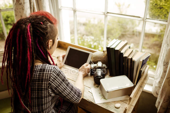 Высокоугольный вид молодой женщины, использующей планшетный компьютер у окна дома — стоковое фото
