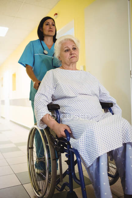 Медсестра толкает пожилого пациента на инвалидном кресле в больнице — стоковое фото