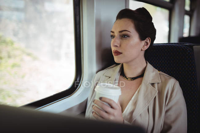 Bella donna in possesso di tazza usa e getta mentre seduto in treno — Foto stock