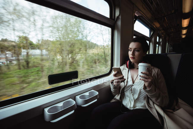 Young woman using mobile phone by window in train — Stock Photo