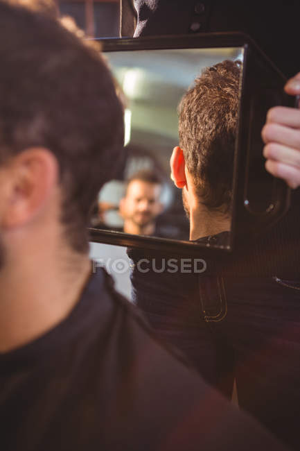 Hairdresser showing man his haircut in mirror at salon — Stock Photo