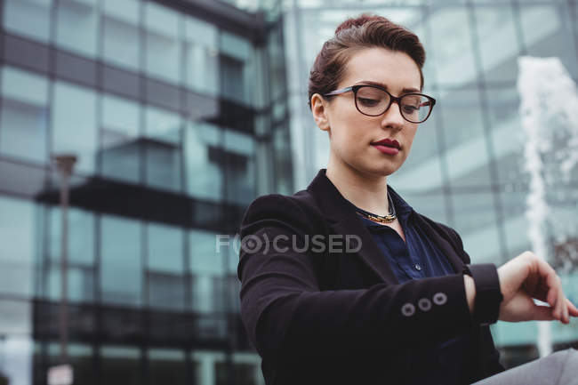 Бізнес-леді перевіряє час проти офісної будівлі — стокове фото