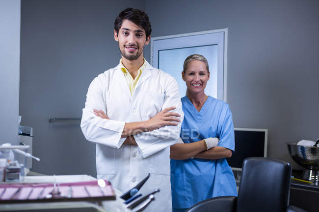 Portrait d'un dentiste souriant et d'une assistante dentaire debout les bras croisés à la clinique dentaire — Photo de stock