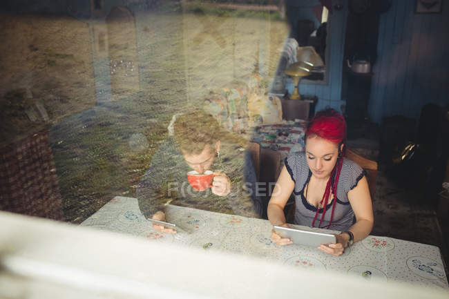 Молода пара використовує цифрові планшети за столом, видно з вікна вдома — стокове фото