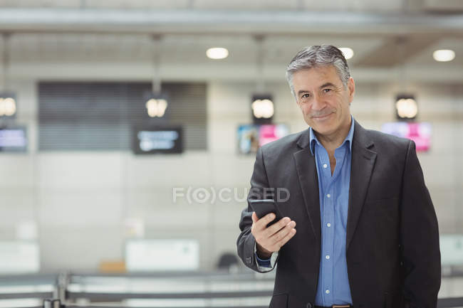 Empresario que usa teléfono móvil en la sala de espera en la terminal del aeropuerto - foto de stock