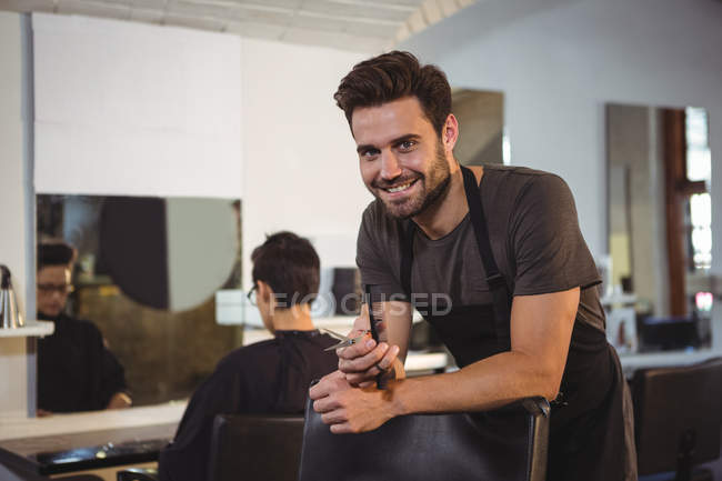 Retrato de cabeleireiro masculino segurando tesoura e pente no salão — Fotografia de Stock