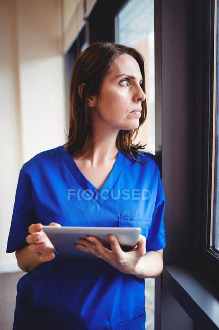 Enfermera sosteniendo tableta digital y mirando a la ventana en el hospital - foto de stock