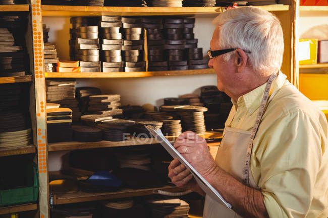 Senior shoemaker writing on clipboard in workshop — Stock Photo