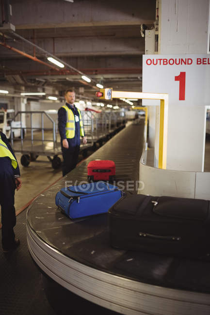 Tripulação de terra do aeroporto descarregando bagagem do carrossel de bagagem no terminal do aeroporto — Fotografia de Stock
