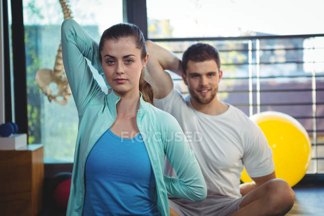 Retrato del hombre y la mujer realizando ejercicio de estiramiento en la clínica - foto de stock