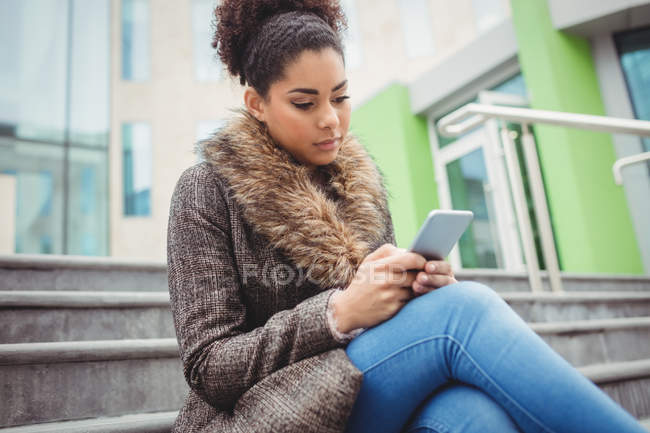 Концентрована жінка використовує телефон, сидячи на кроках — стокове фото