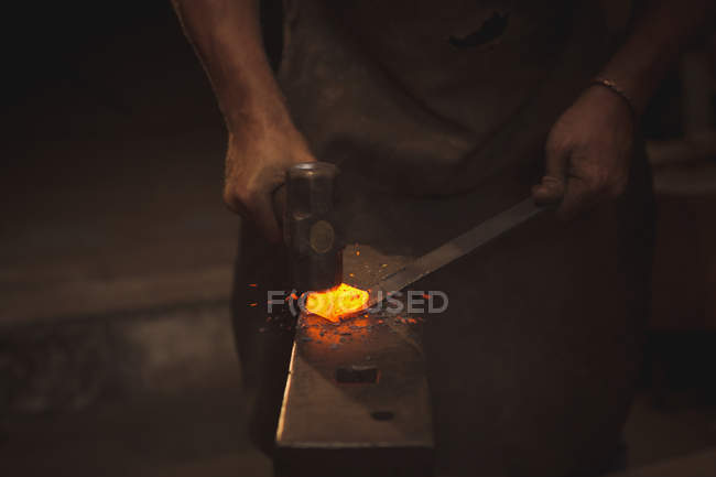 Blacksmith working on a heated iron rod in workshop — Stock Photo