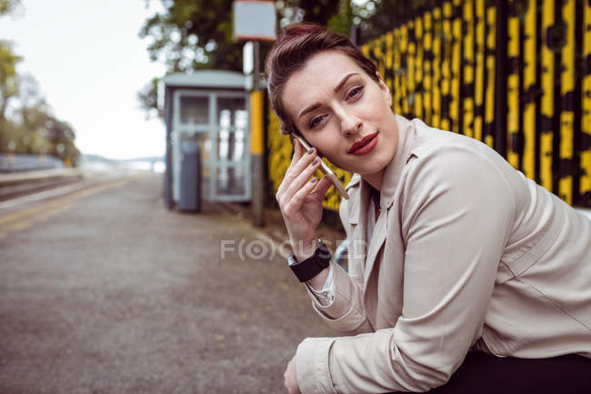 Retrato de una hermosa mujer hablando por teléfono en la plataforma de la estación de tren - foto de stock