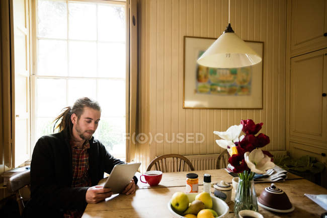 Молодий чоловік використовує цифровий планшет, сидячи за столом — стокове фото
