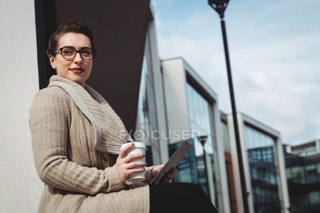 Жінка тримає одноразову чашку і цифровий планшет проти будівництва — стокове фото