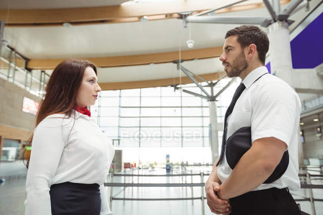 Piloto y auxiliar de vuelo interactuando entre sí en la terminal del aeropuerto - foto de stock