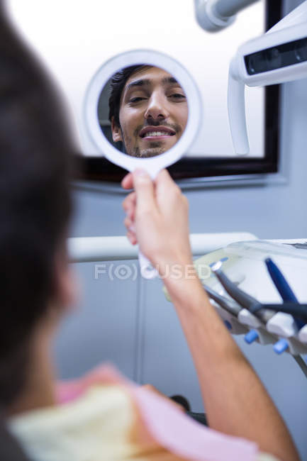 Задний вид улыбающегося пациента, сидящего на стоматологическом стуле и смотрящего в зеркало в клинике — стоковое фото