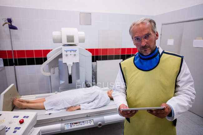 Médico sosteniendo tableta digital y paciente acostado en máquina de rayos X en el hospital - foto de stock