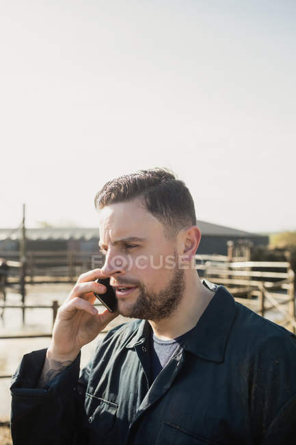 Jovem agricultor falando no celular na fazenda contra o céu — Fotografia de Stock