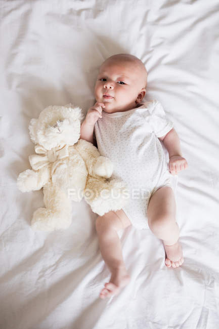 Blick von oben auf entzückendes Baby, das mit Teddybär im Bett liegt — Stockfoto