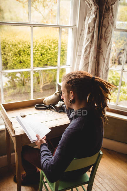 Man reading book while sitting on chair at home — Stock Photo