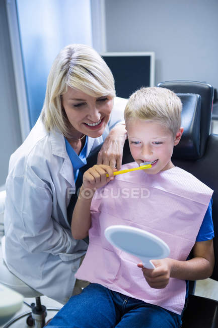 Dentista che assiste il giovane paziente mentre si lava i denti in clinica dentale — Foto stock