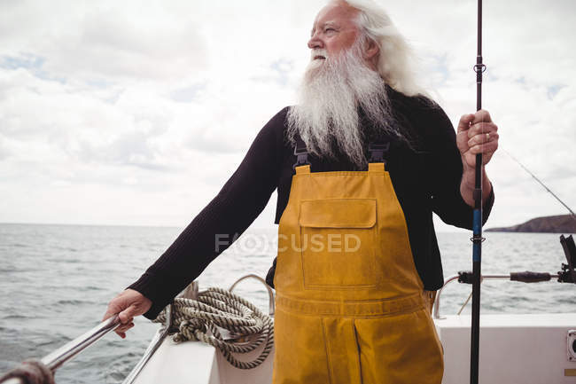 Pensativo pescador senior de pie en el barco y la celebración de caña de pescar - foto de stock
