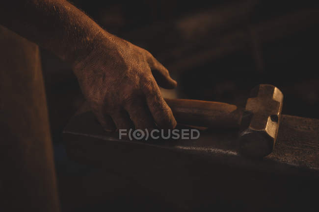 Mano de herrero sosteniendo martillo en taller - foto de stock