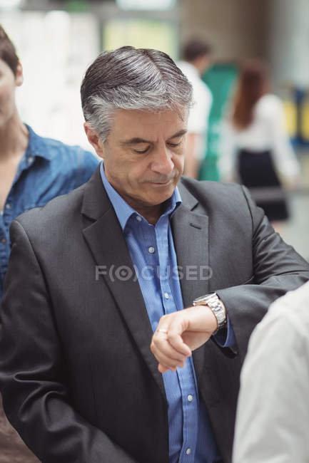 Empresario comprobando el tiempo mientras está de pie en cola en la terminal del aeropuerto - foto de stock