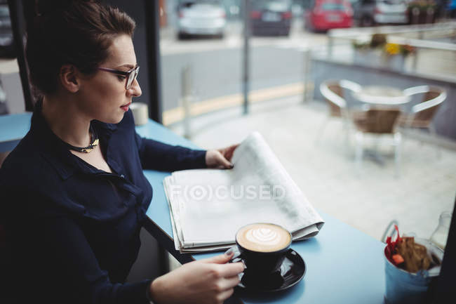 Donna d'affari con caffè tazza di lettura giornale in caffè — Foto stock