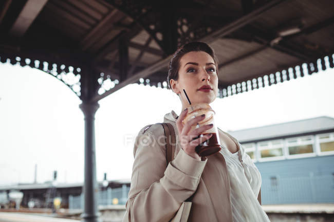 Молода жінка тримає напій, стоячи на залізничній станції — стокове фото
