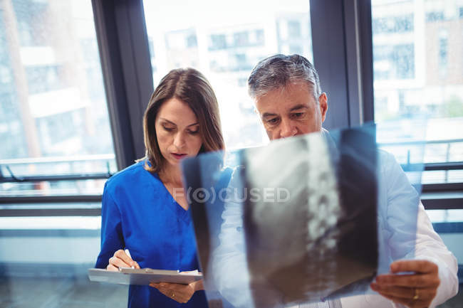 Médico examinando rayos X mientras la enfermera escribe en portapapeles en el hospital - foto de stock