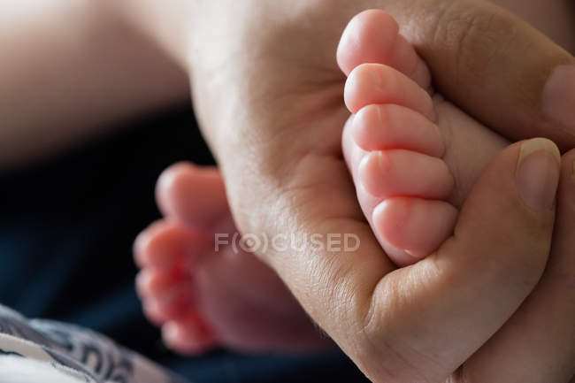 Image recadrée de la mère tenant les pieds de bébé à la maison — Photo de stock