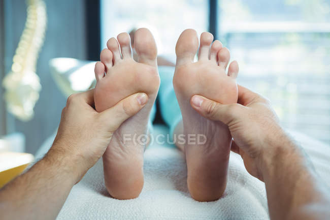 Обрезанное изображение мужского физиотерапевта, делающего массаж ступней пациентке в клинике — стоковое фото