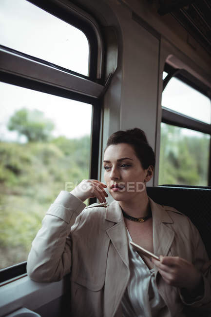 Mujer reflexiva sosteniendo el teléfono móvil mientras está sentado en el tren - foto de stock