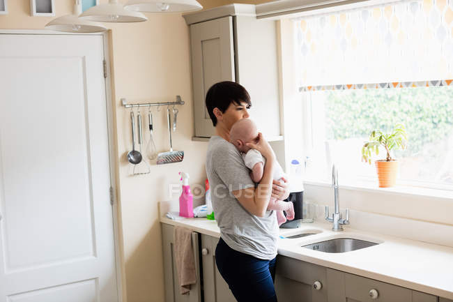 Mãe segurando seu bebê na cozinha em casa — Fotografia de Stock