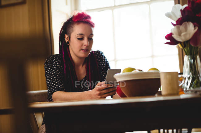 Молода жінка, використовуючи мобільний телефон, сидячи за столом вдома — стокове фото