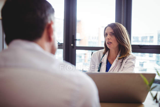 Female doctor at desk talking to patient in hospital — Stock Photo