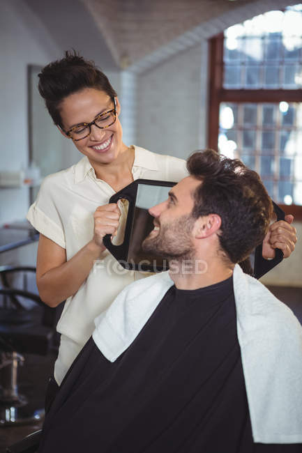 Sorrindo cabeleireiro feminino mostrando o homem seu corte de cabelo no espelho no salão — Fotografia de Stock