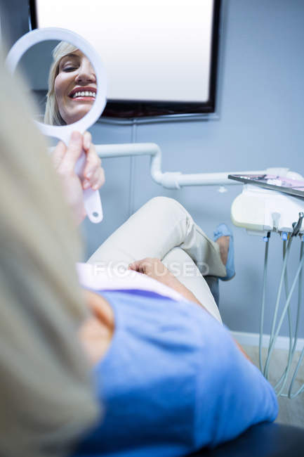 Patiente vérifiant ses dents dans un miroir à la clinique dentaire — Photo de stock