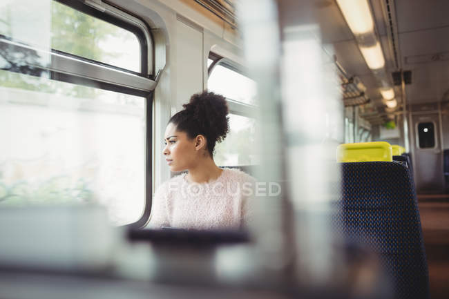 Nachdenkliche kluge Frau schaut durch Fenster, während sie im Zug sitzt — Stockfoto