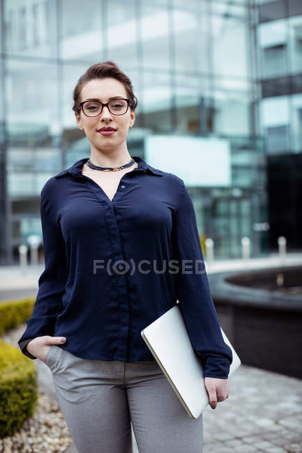 Портрет впевненої бізнес-леді з ноутбуком, що стоїть за межами офісної будівлі — стокове фото