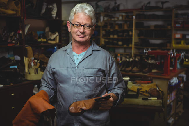 Zapatero maduro sosteniendo una bota y pieza de material en el taller - foto de stock