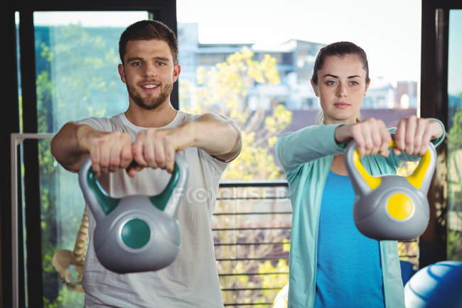 Hombre y mujer haciendo ejercicio con campanas en la clínica - foto de stock
