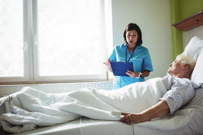 Enfermeira interagindo sobre um relatório com paciente sênior no hospital — Fotografia de Stock