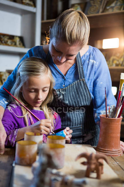 Жіночий гончар допомагає дівчині в живописі в керамічній майстерні — стокове фото