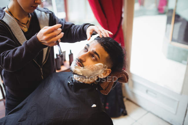 Un homme se fait raser la barbe avec un rasoir dans un salon de coiffure — Photo de stock