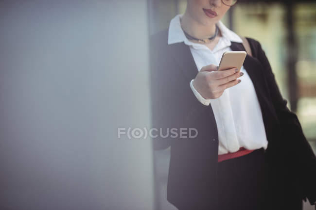 Молода жінка, використовуючи мобільний телефон, спираючись на стіну — стокове фото