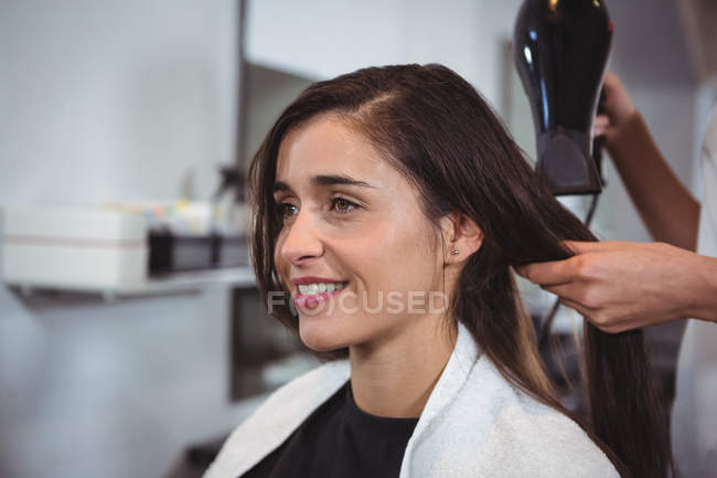 Mujer secándose el pelo con secador de pelo en la peluquería - foto de stock